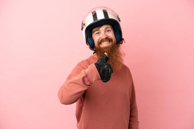 Young reddish caucasian man with a motorcycle helmet isolated on pink background giving a thumbs up gesture