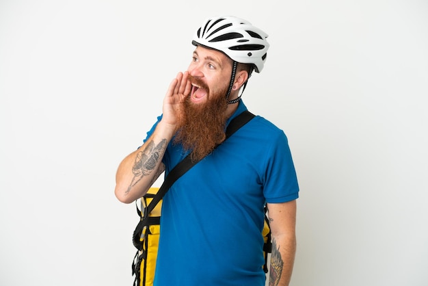 Young reddish caucasian man with thermal backpack isolate don white background shouting with mouth wide open to the side