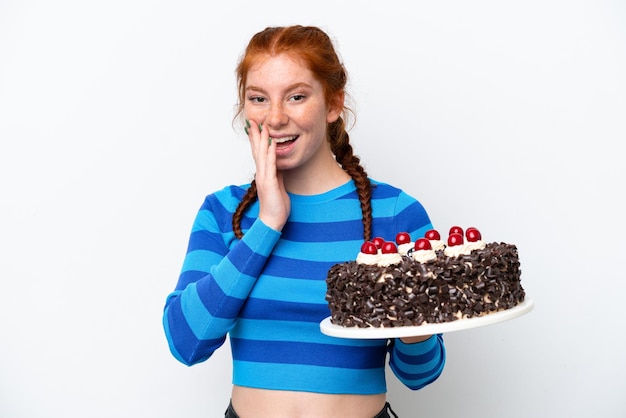 Foto giovane donna rossastra che tiene la torta di compleanno isolata su sfondo bianco con espressione facciale sorpresa e scioccata