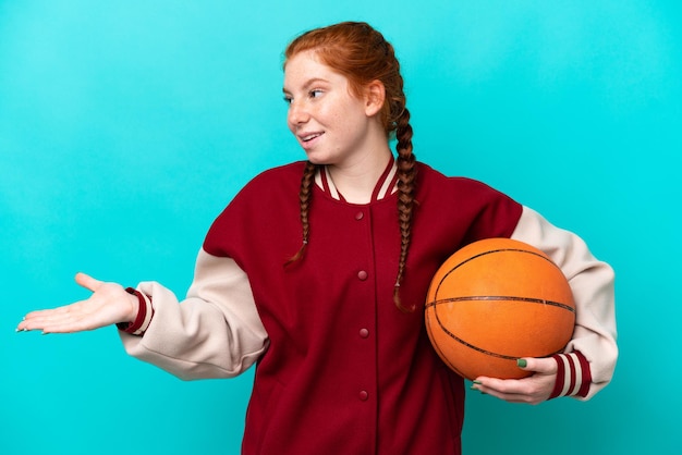 Young reddish woman playing basketball isolated on blue background with surprise expression while looking side