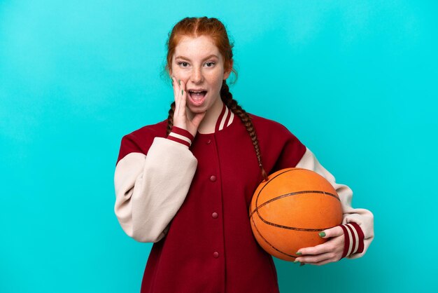 Young reddish woman playing basketball isolated on blue background with surprise and shocked facial expression