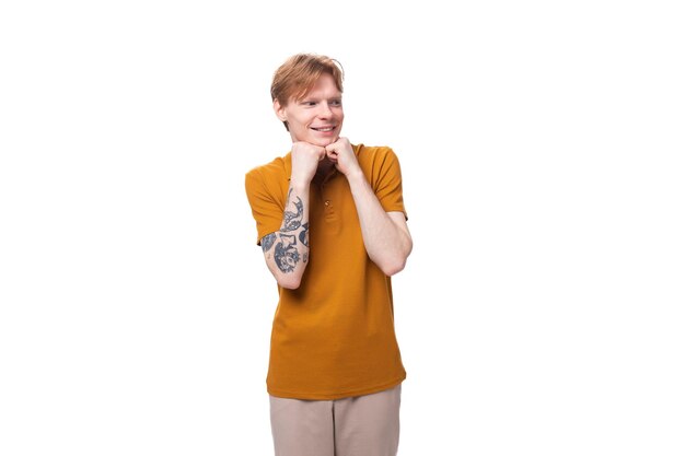 Young redhaired caucasian student man with a tattoo dressed in a mustard tshirt on a white