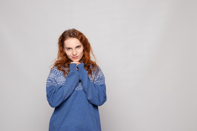 Young redhaired girl in a knitted sweater on a white background