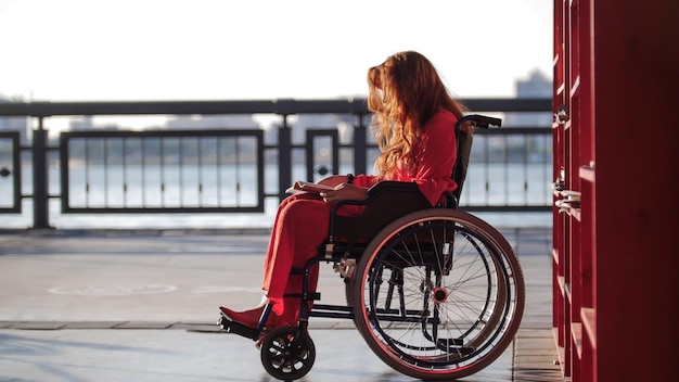 Young redhaired girl reading a book in a wheelchair on the street