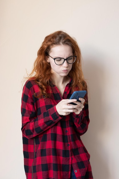 Young redhaired girl talking on the phone on a light background