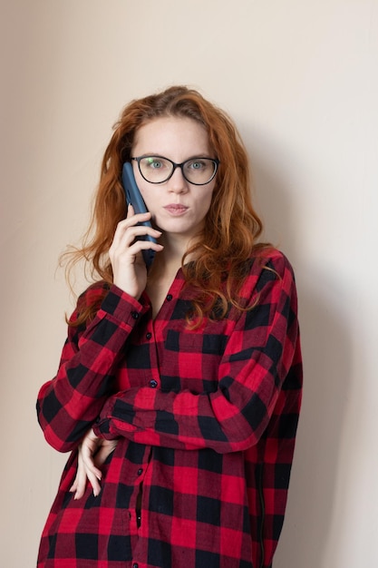 Young redhaired girl talking on the phone on a light background