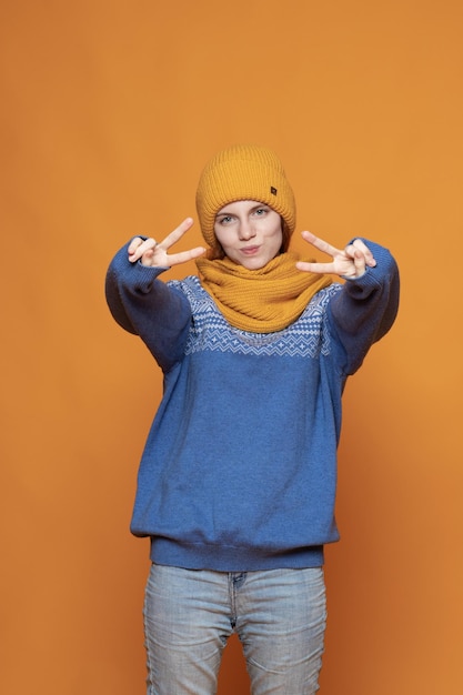 Young redhaired girl in a warm hat and a knitted sweater on a yellow background