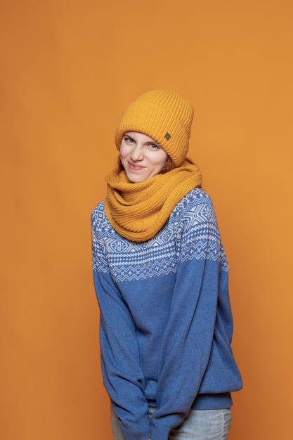 Young redhaired girl in a warm hat and a knitted sweater on a yellow background