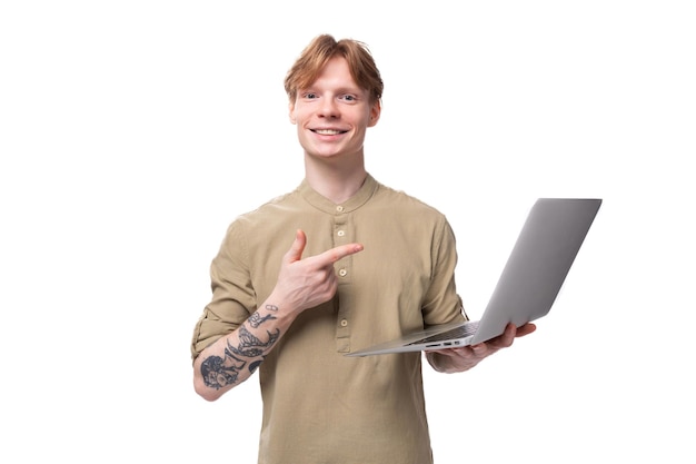A young redhaired guy in glasses and a brown shirt holds a laptop in his hands it specialist stands
