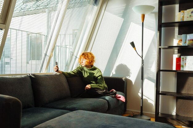 Young redhaired woman in living room on sofa using phone