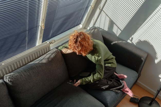 Photo young redhaired woman in living room on sofa using phone