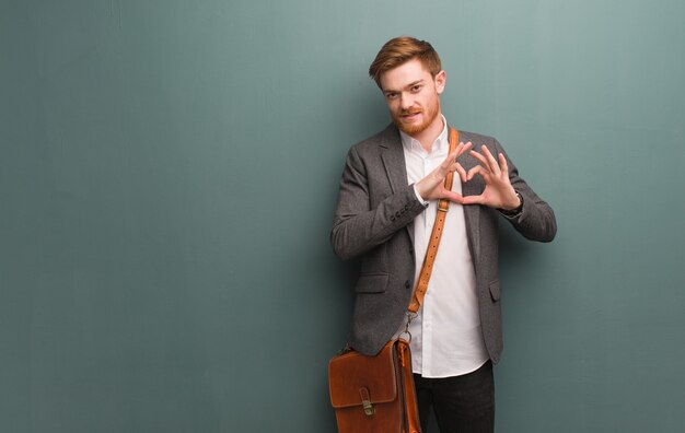 Young redhead business man doing a heart shape with hands