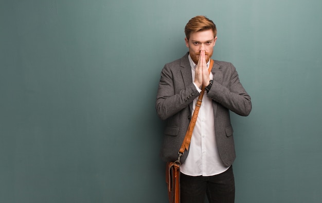 Young redhead business man praying very happy and confident