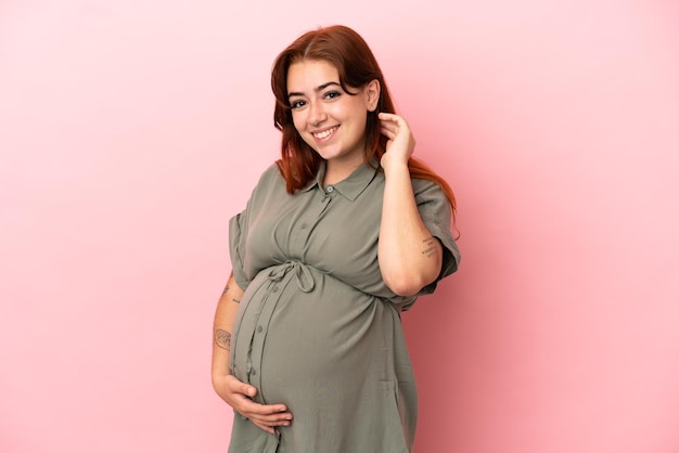 Young redhead caucasian woman isolated on pink background pregnant and happy