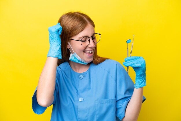 Young redhead dentist woman isolated on yellow background celebrating a victory