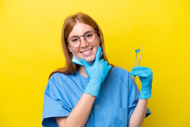 Young redhead Dentist woman isolated on yellow background happy and smiling