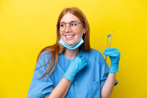 笑顔で見上げる黄色の背景に分離された若い赤毛歯科医の女性