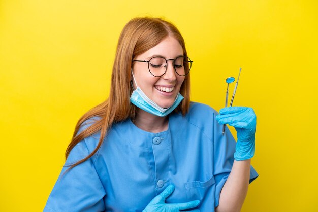 Young redhead dentist woman isolated on yellow background smiling a lot