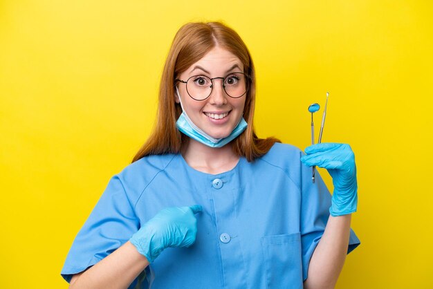 Young redhead dentist woman isolated on yellow background with surprise facial expression