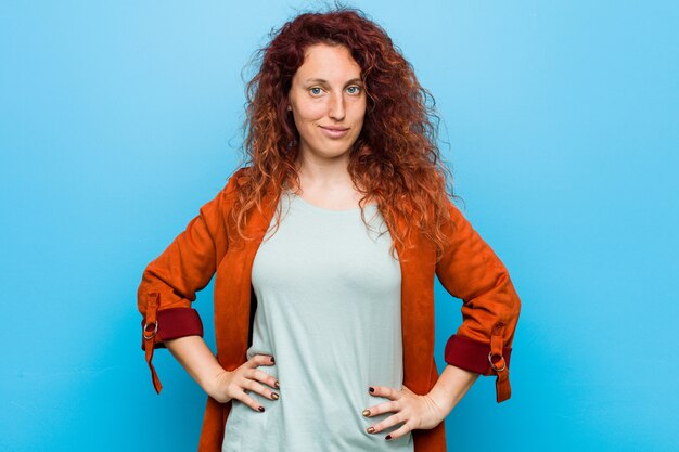 Young redhead elegant woman confident keeping hands on hips.