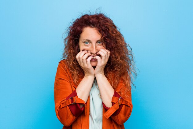 Young redhead elegant woman laughing about something, covering mouth with hands.