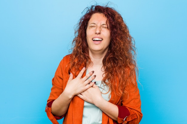 Young redhead elegant woman laughing keeping hands on heart, concept of happiness.