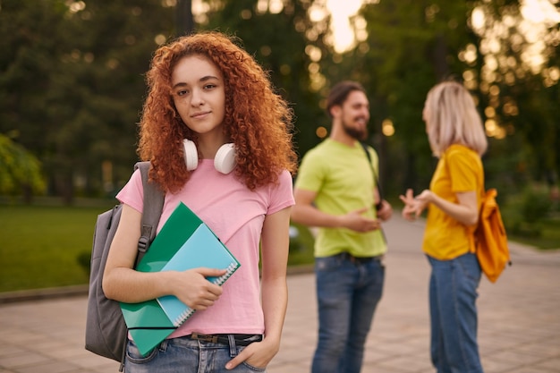 Foto giovane studentessa rossa in piedi nel campus vicino agli amici