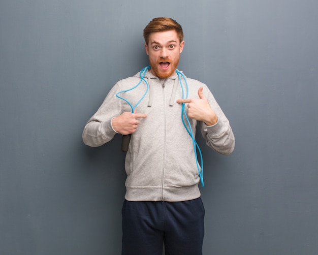 Young redhead fitness man surprised, feels successful and prosperous. He is holding a jump rope.