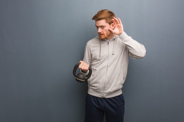 Il giovane uomo di forma fisica di redhead prova ad ascoltare un gossip.