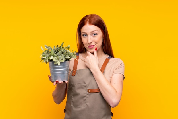 Young redhead gardener woman holding a plant laughing