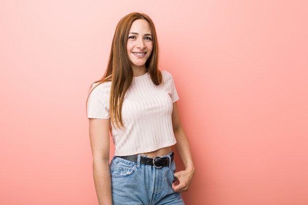 Foto giovane donna dello zenzero di redhead contro una parete dentellare felice, sorridente e allegra.