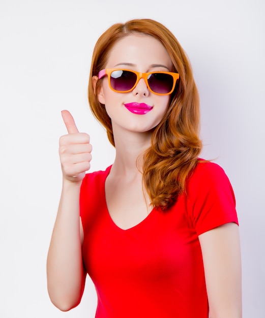 Young redhead girl in red dress in sunglasses on white