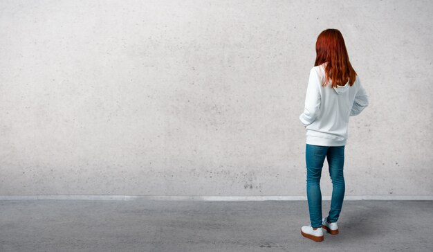 Young redhead girl in an urban white sweatshirt with glasses looking back and standing