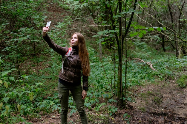 Young redhead long hair woman making photos during travel in forest