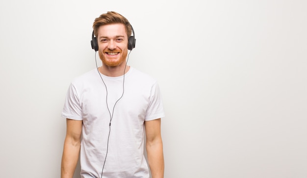 Uomo giovane rossa allegro con un grande sorriso. ascoltare musica con le cuffie.