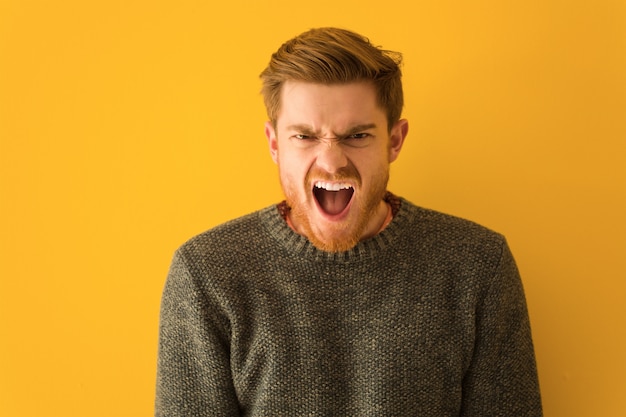 Young redhead man face closeup screaming very angry and aggressive