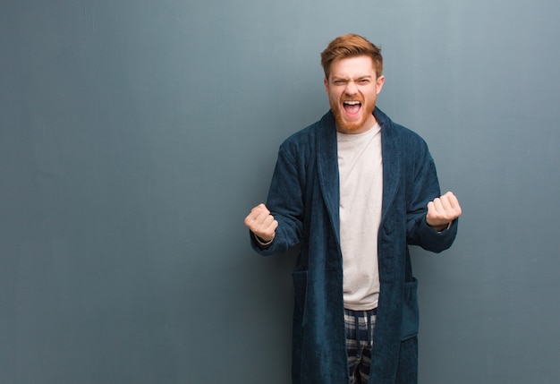 Young redhead man in pajama surprised and shocked