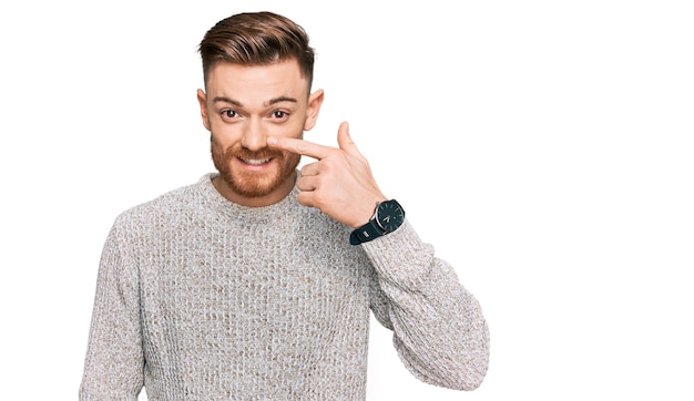 Young redhead man wearing casual winter sweater pointing with hand finger to face and nose smiling cheerful beauty concept