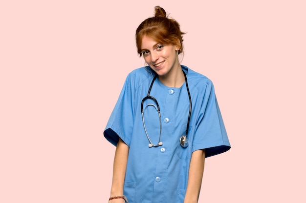 Young redhead nurse happy and smiling over pink background