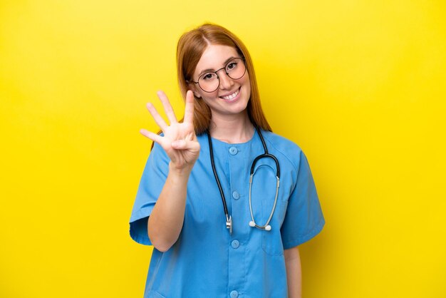 幸せな黄色の背景に分離された若い赤毛の看護師の女性と指で 4 つを数える