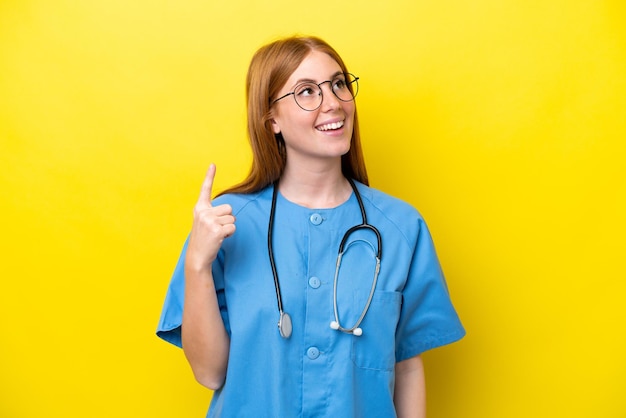 Young redhead nurse woman isolated on yellow background pointing up and surprised