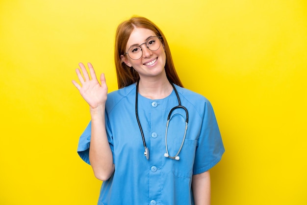 Young redhead nurse woman isolated on yellow background saluting with hand with happy expression