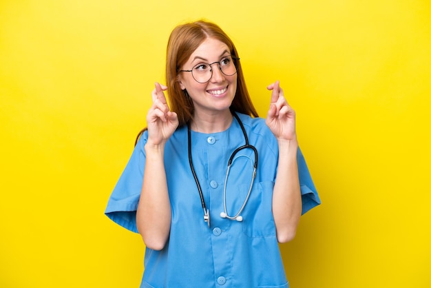 Young redhead nurse woman isolated on yellow background with fingers crossing