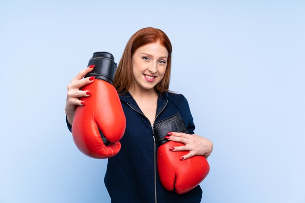 Young redhead sport woman over isolated blue background with boxing gloves