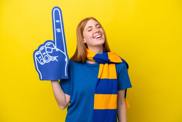 Young redhead sports fan woman isolated on yellow background laughing