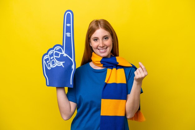 Young redhead sports fan woman isolated on yellow background
making money gesture