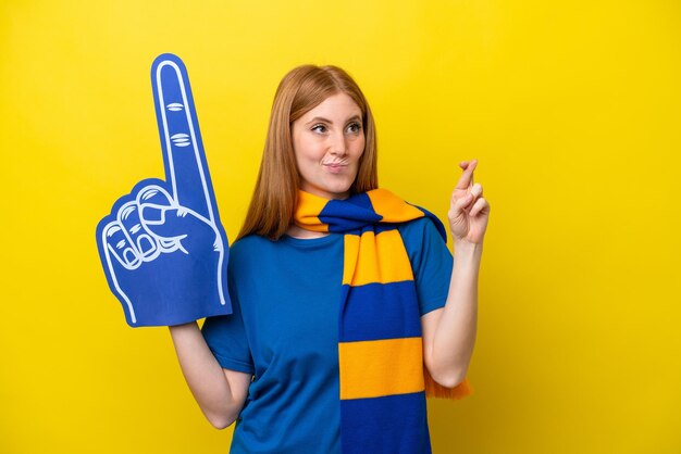 Young redhead sports fan woman isolated on yellow background\
with fingers crossing and wishing the best