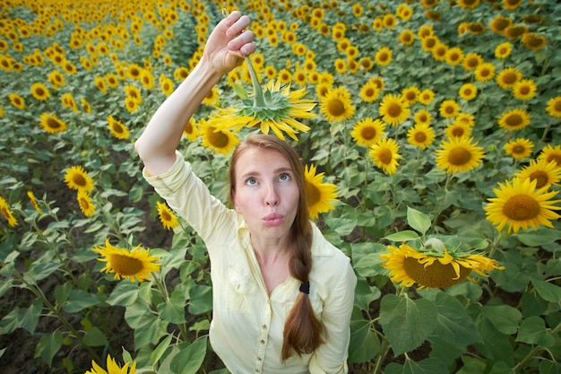 Young redhead woman has fun in summer sunflower field