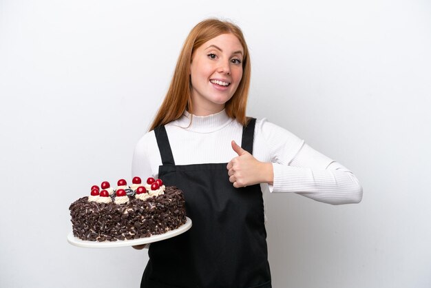 Young redhead woman holding birthday cake isolated on white background giving a thumbs up gesture