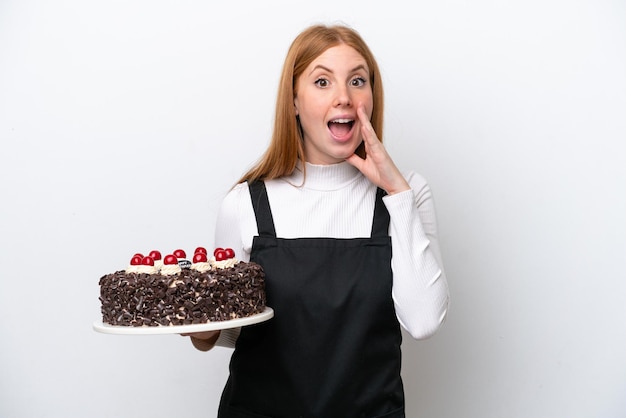 Young redhead woman holding birthday cake isolated on white background with surprise and shocked facial expression